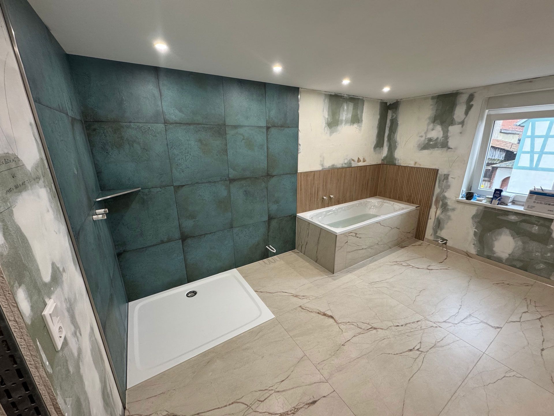 Badezimmerrenovierung: türkis geflieste Dusche, weiße Duschwanne, Badewanne, heller Fliesenboden, unfertige Wände.