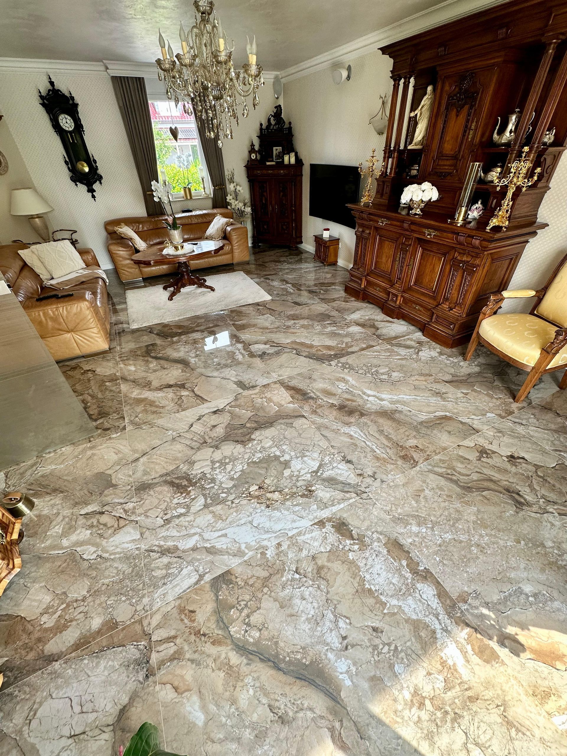 Wohnzimmer mit kunstvollen Holzmöbeln, Kronleuchter und gemustertem Marmorboden.