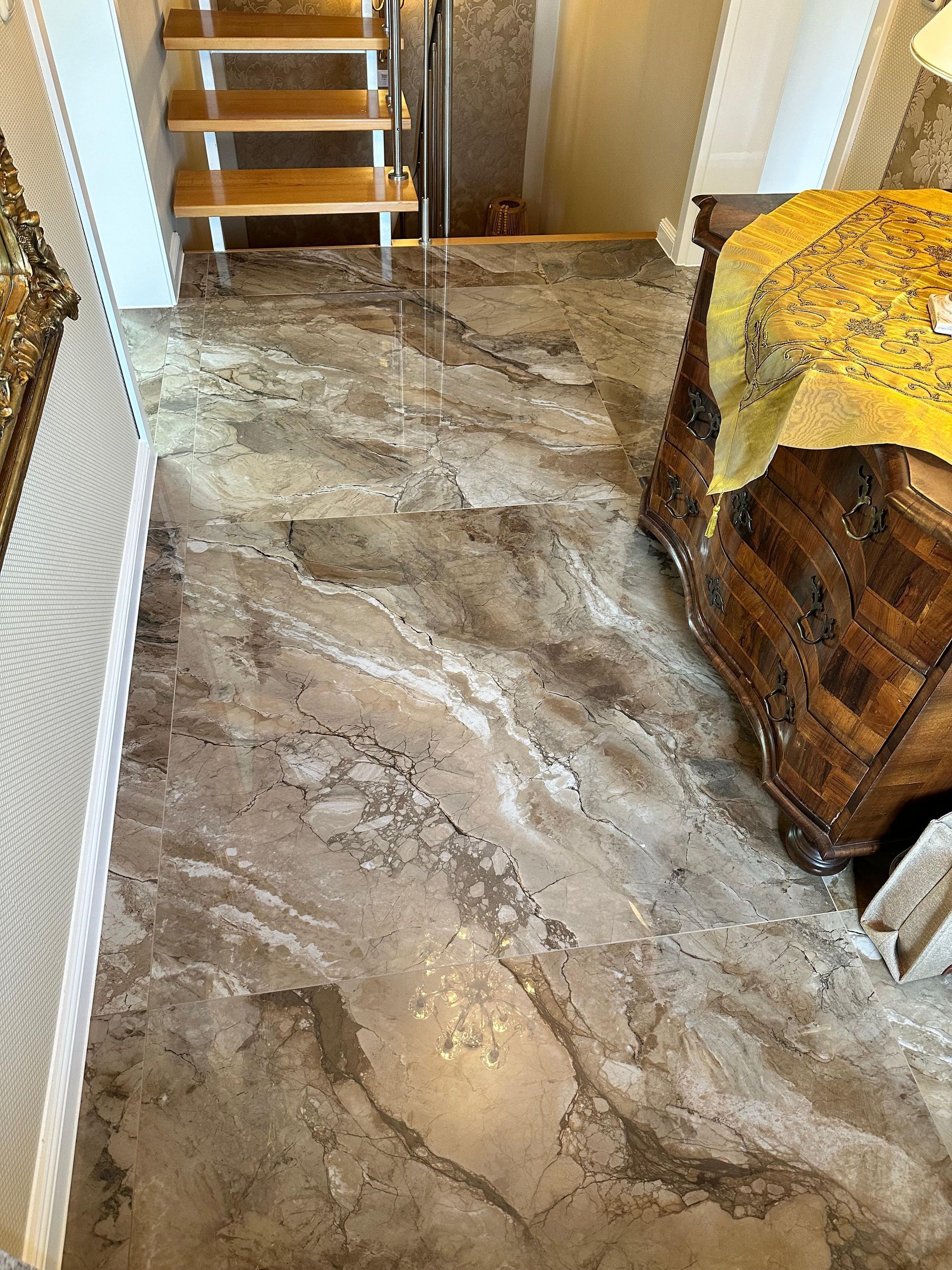 Marmorfliesenboden mit Holztreppe und verzierter Holztruhe.