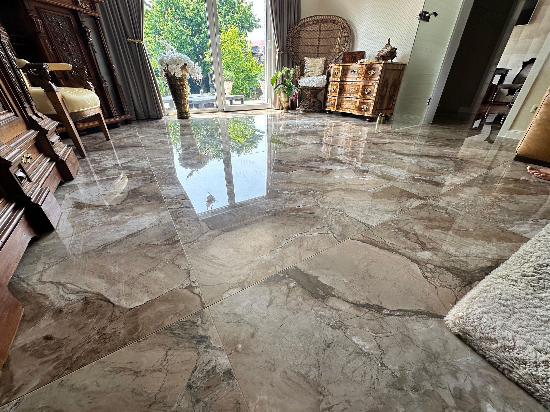 Glänzender, gemusterter Marmorboden, der das Licht reflektiert; Holzmöbel und ein großes Fenster im Hintergrund.