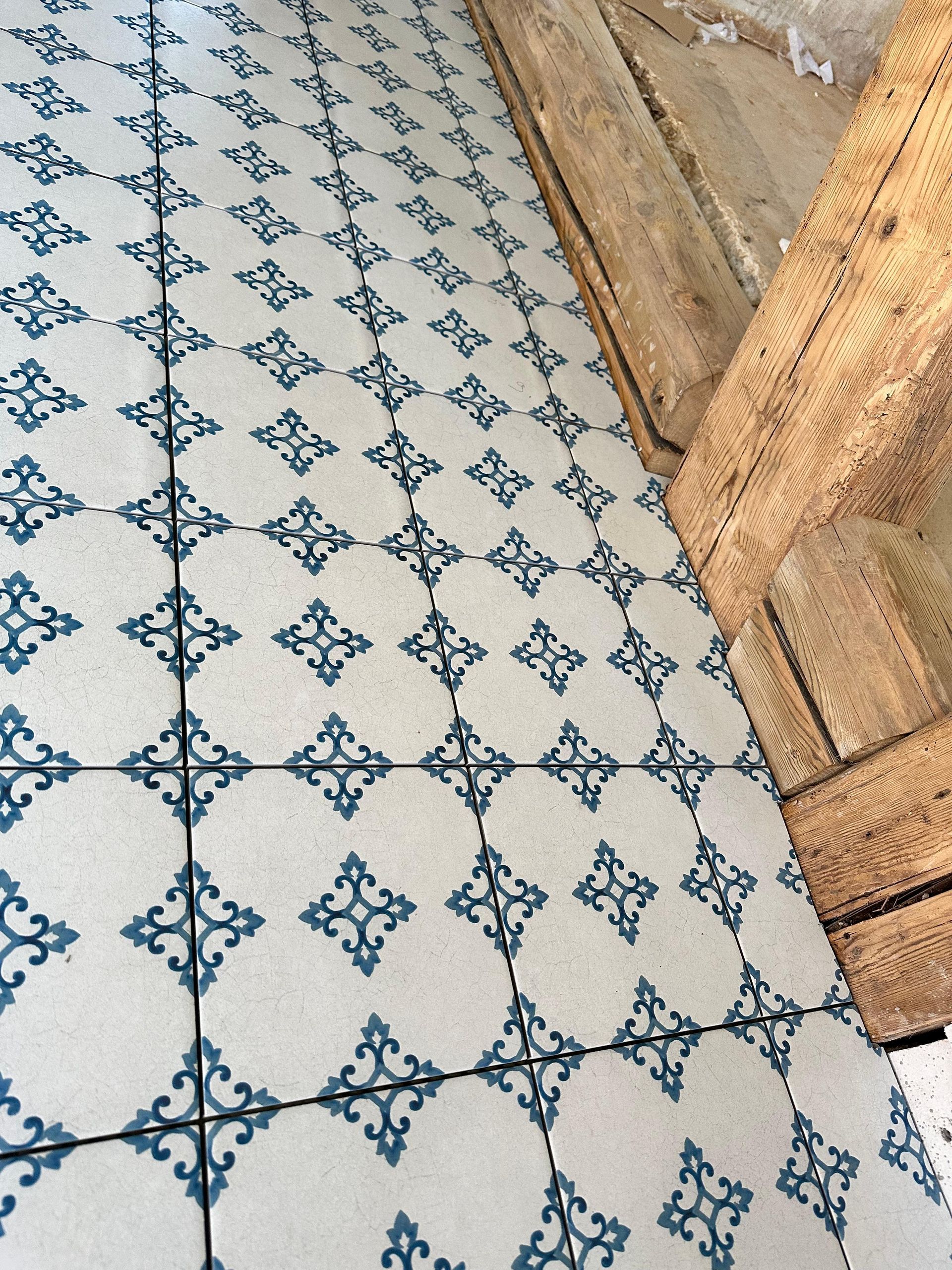 Blau-weiß gemusterte Bodenfliesen neben verwittertem Holz.