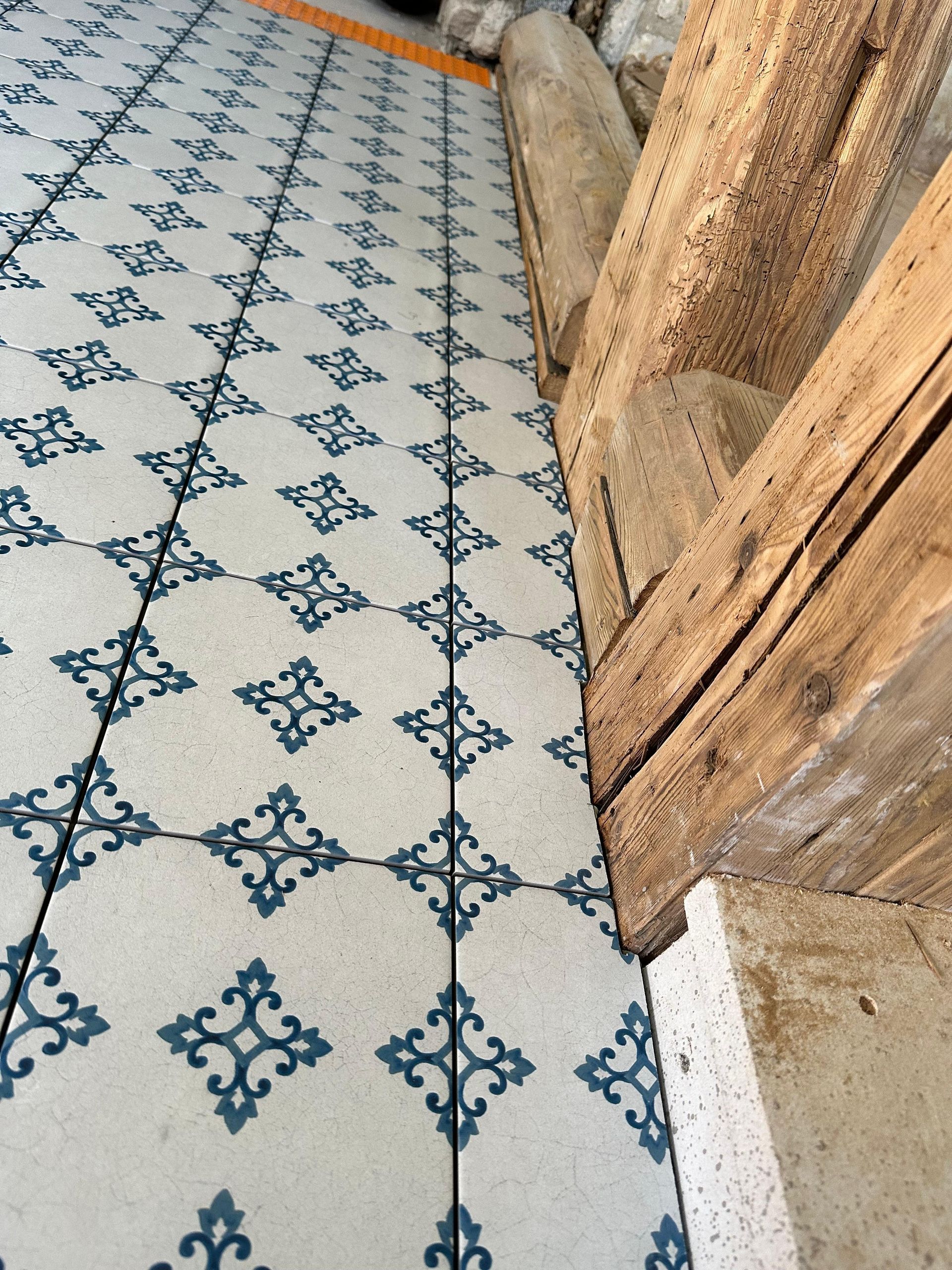 Blau-weiß gemusterter Fliesenboden neben verwitterten Holzbalken.