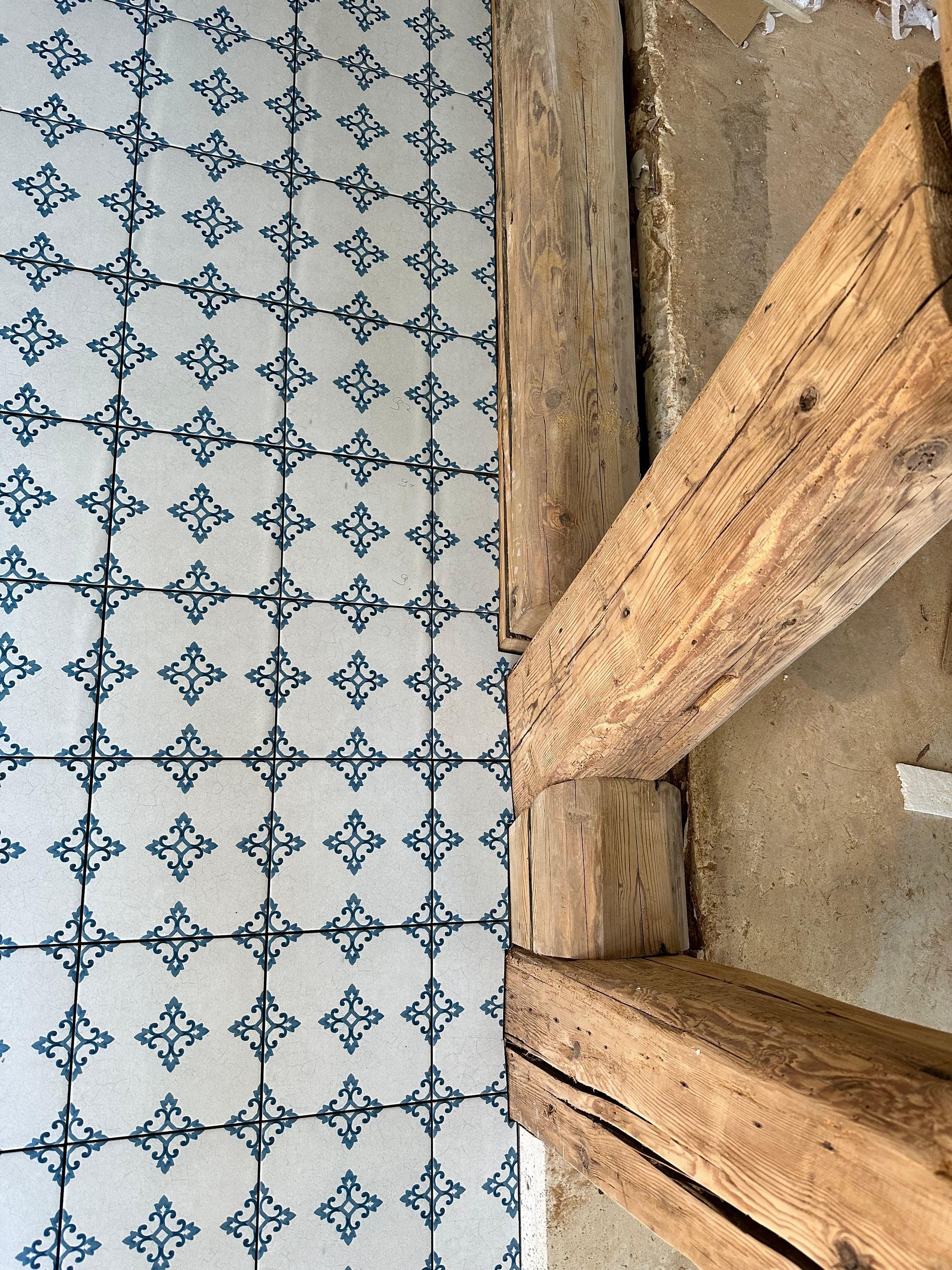 Blau-weiß gemusterter Fliesenboden neben verwitterten Holzbalken und -wand.