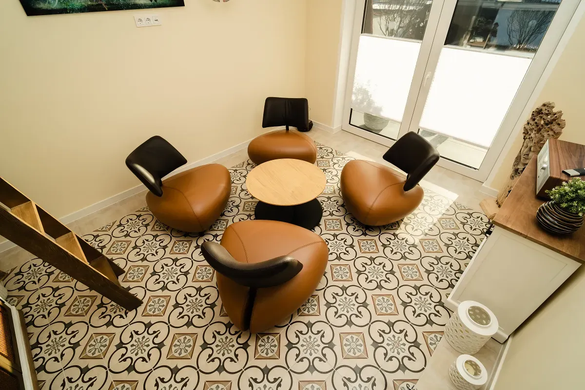 Kleine Sitzecke mit vier braunen Stühlen um einen runden Tisch auf gemustertem Fliesenboden.