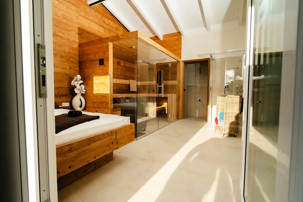 Spa-Interieur mit Holzsauna, Glasdusche, Bett und weißen Fliesen.
