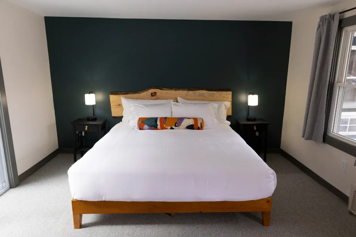 Neatly made bed with white bedding in a modern bedroom with dark accent wall and bedside lamps