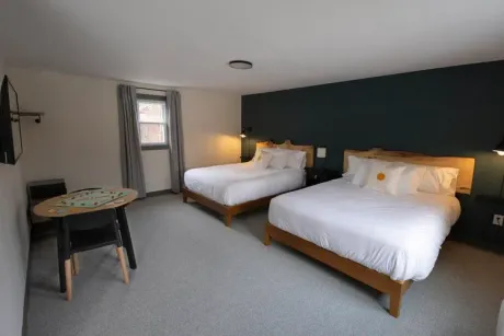 Modern hotel room with two white beds, a small table, and a dark accent wall