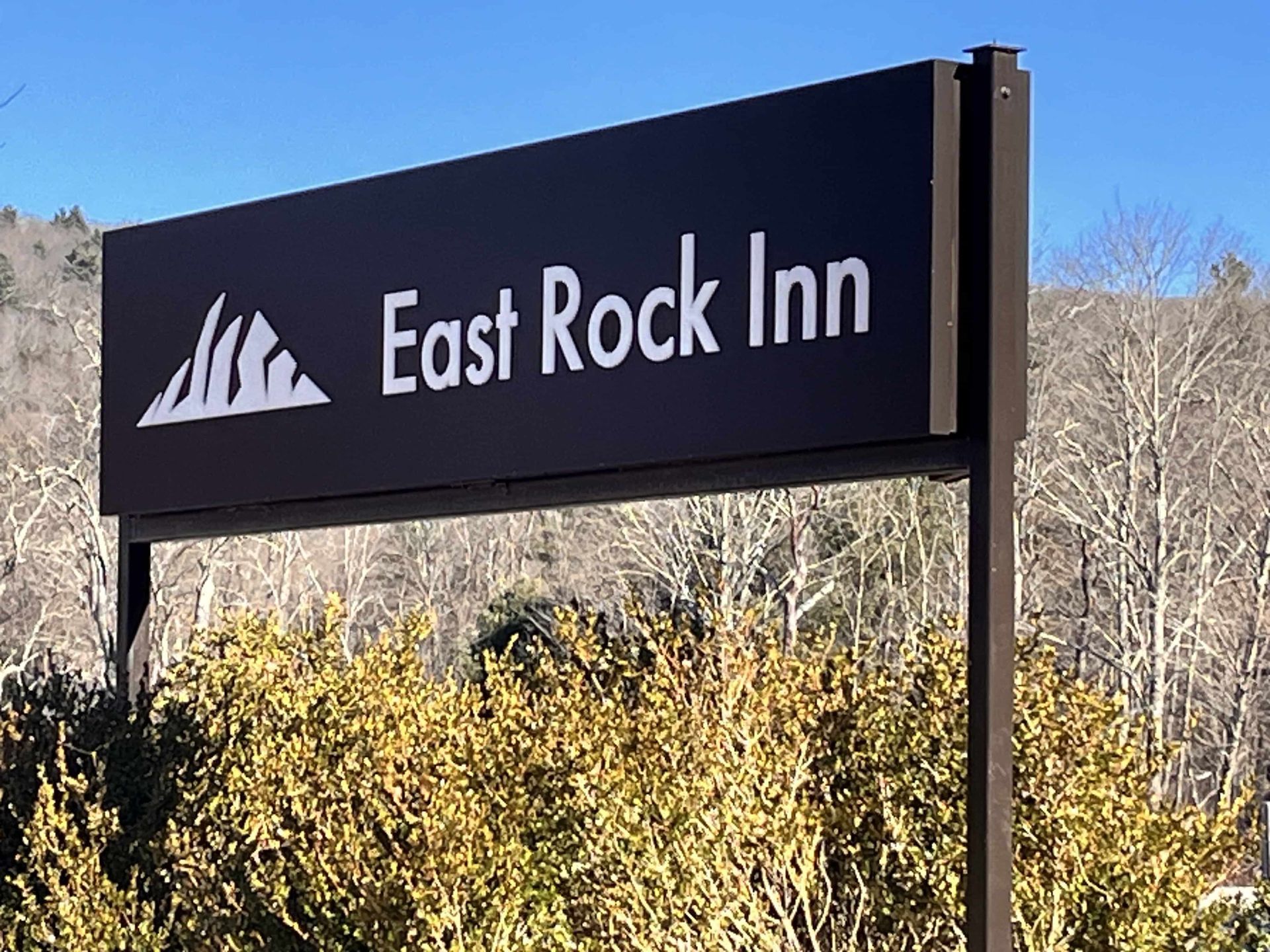 East Rock Inn sign on a post outdoors with mountains logo against trees and blue sky