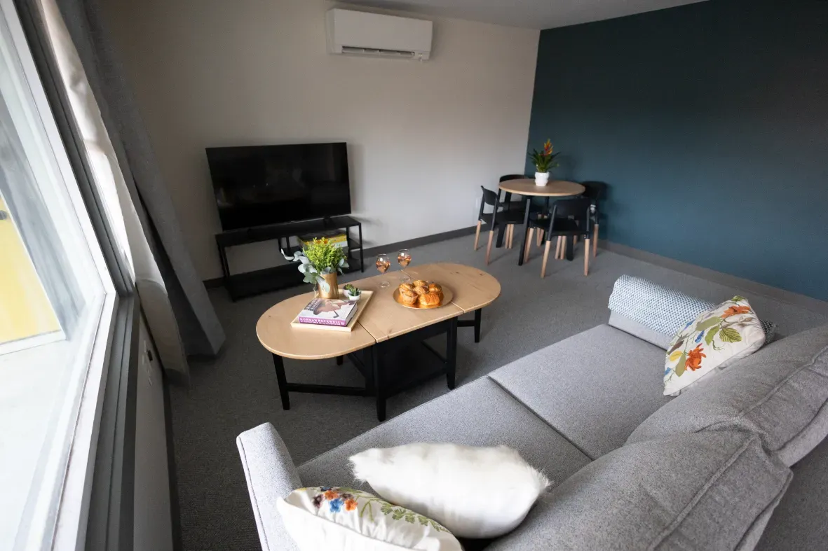 Modern living room with gray sectional sofa, coffee table, TV, and small dining area by a blue wall
