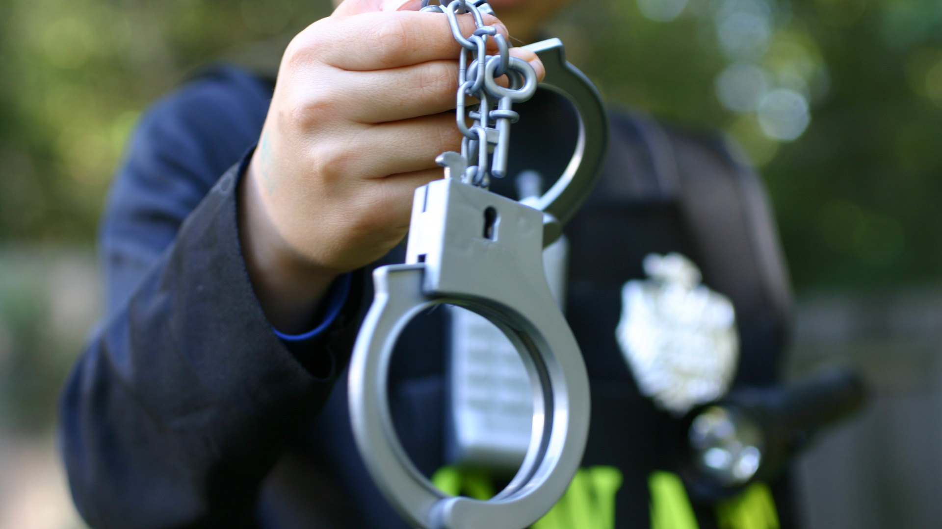 A person in a police uniform holds silver handcuffs and keys in their outstretched hand.