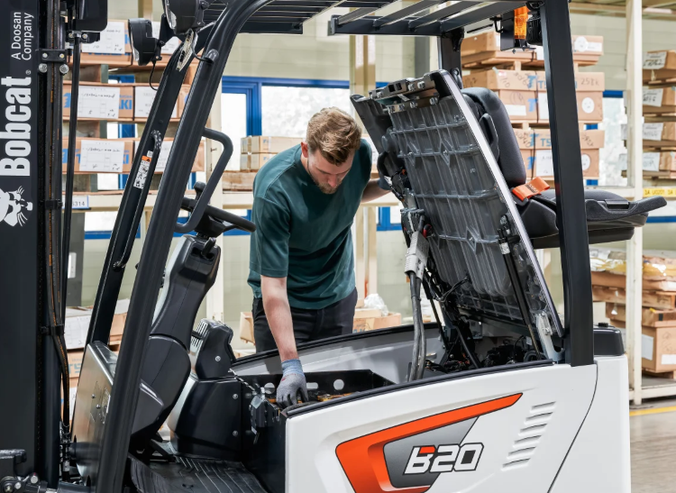 Mechanic working on a Bobcat B20 forklift in a warehouse.