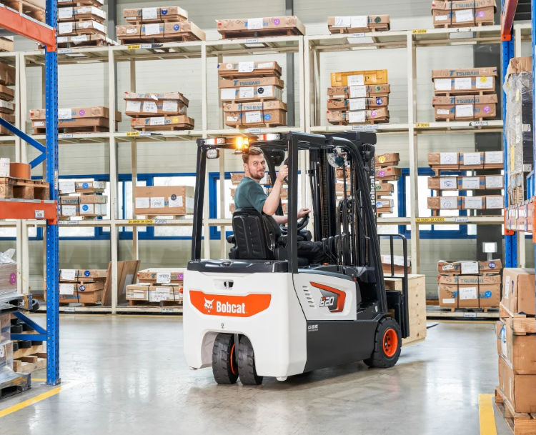 Forklift operator in a warehouse with shelves of boxes.