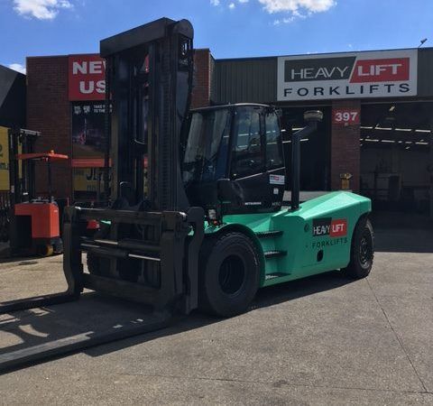 A green forklift is parked in front of a building that says heavy lift forklifts.