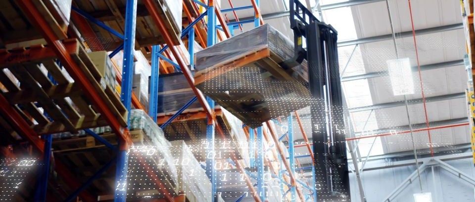 A forklift mast lifting a pallet of goods in a warehouse with shelving