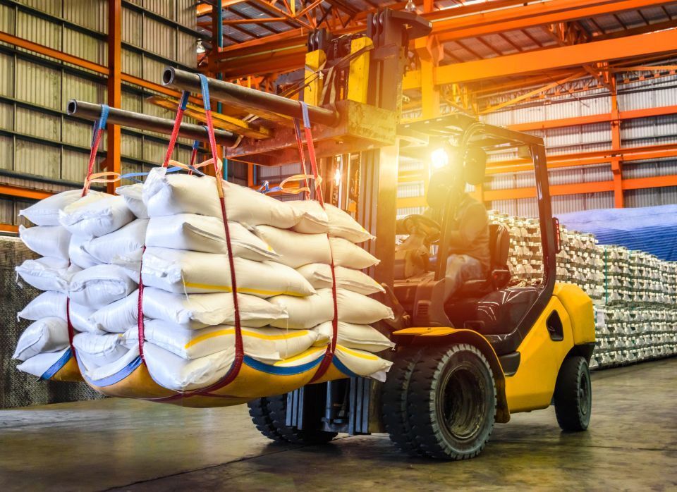 Yellow forklift carrying stacks of sugar inside a food processing facility.