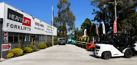 A row of forklifts are parked in front of Heavy Lift Forklifts Building.