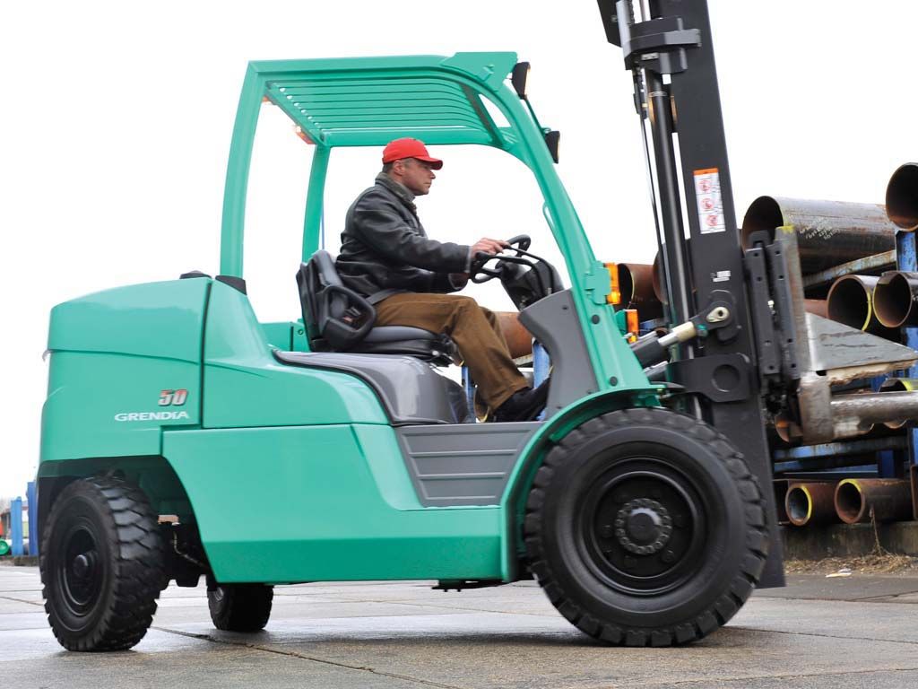 A man is driving a green forklift in a parking lot