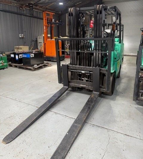 A green mitsubishi forklift for sale is parked in a warehouse with other forklifts