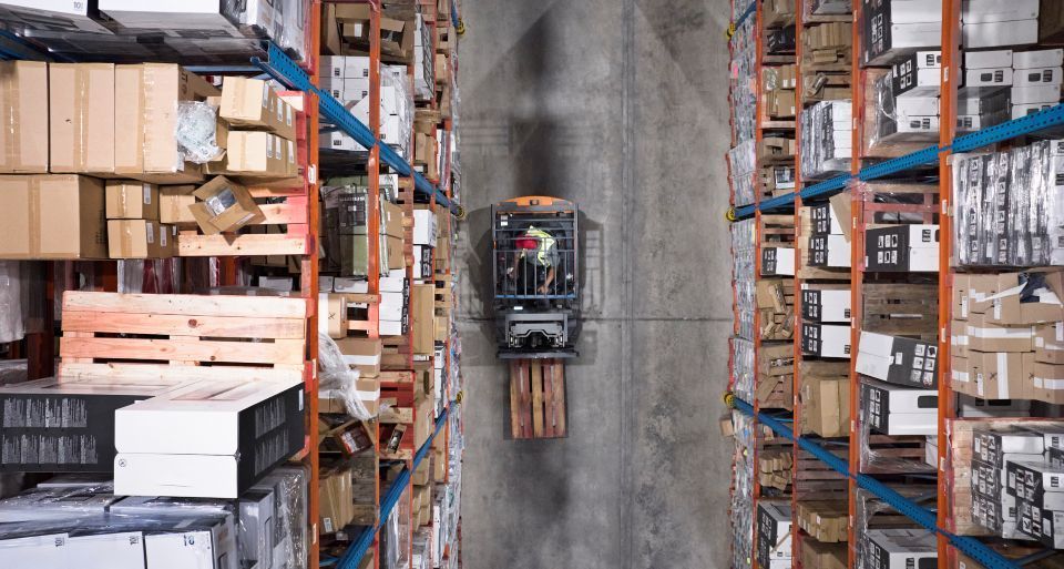 Overhead view of a forklift in a warehouse aisle surrounded by shelves filled with boxes.