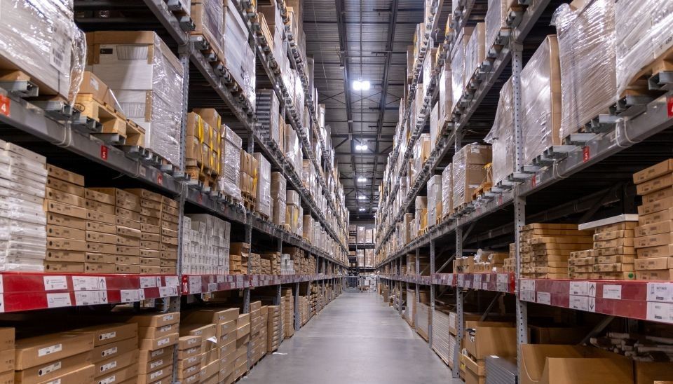Rows of shelves filled with boxes in a warehouse, wide aisle.