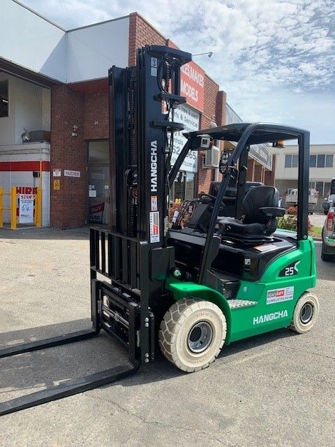 a green forklift is parked in front of a building 