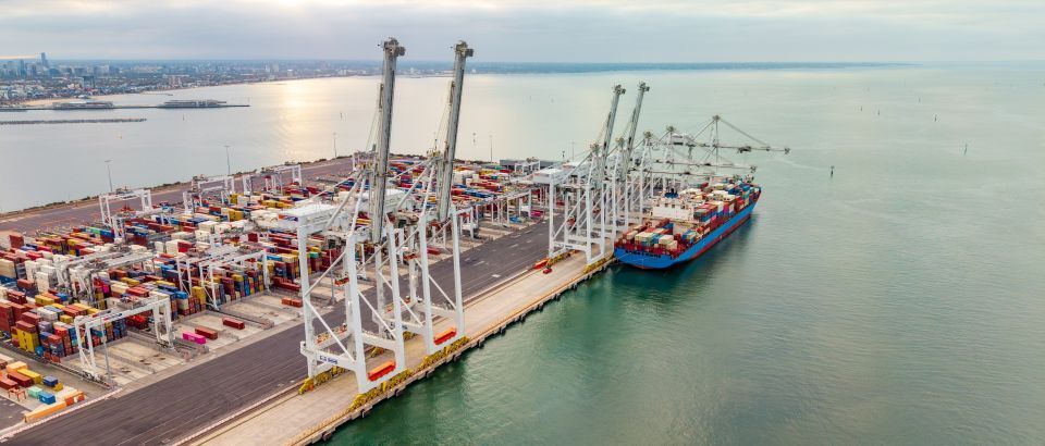 Port Melbourne: Container port with cranes and a cargo ship docked beside stacked shipping containers at sunset