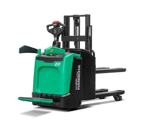 Green and black electric stand-up forklift with raised forks, indoors, ready for use.