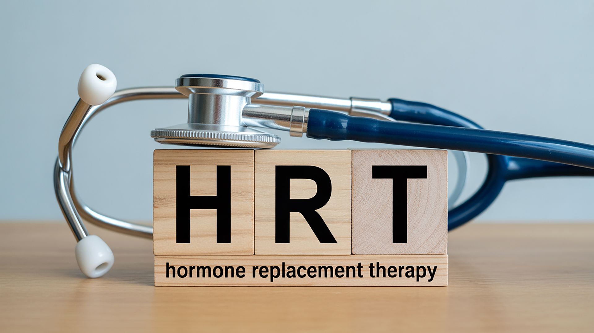 Wooden blocks spelling HRT for hormone replacement therapy next to a medical stethoscope.