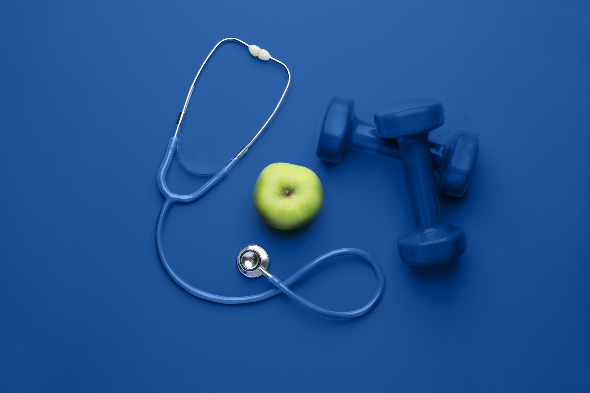 Weight Loss Services concept with an apple, dumbbells, and stethoscope on a blue background. Weight Loss Services concept with an apple, dumbbells, and stethoscope on a blue background.