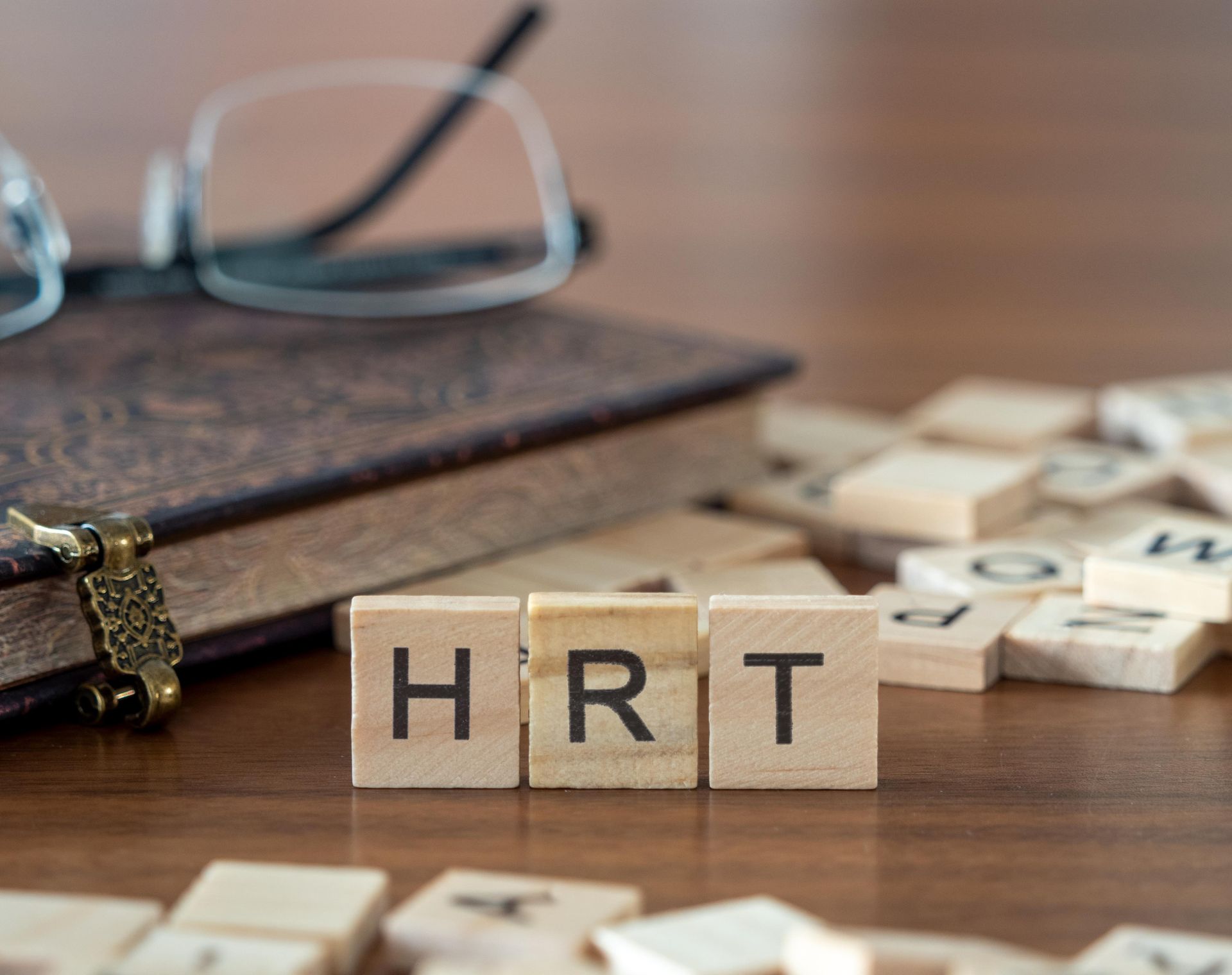 Wooden letter tiles spelling HRT beside eyeglasses on a leather book