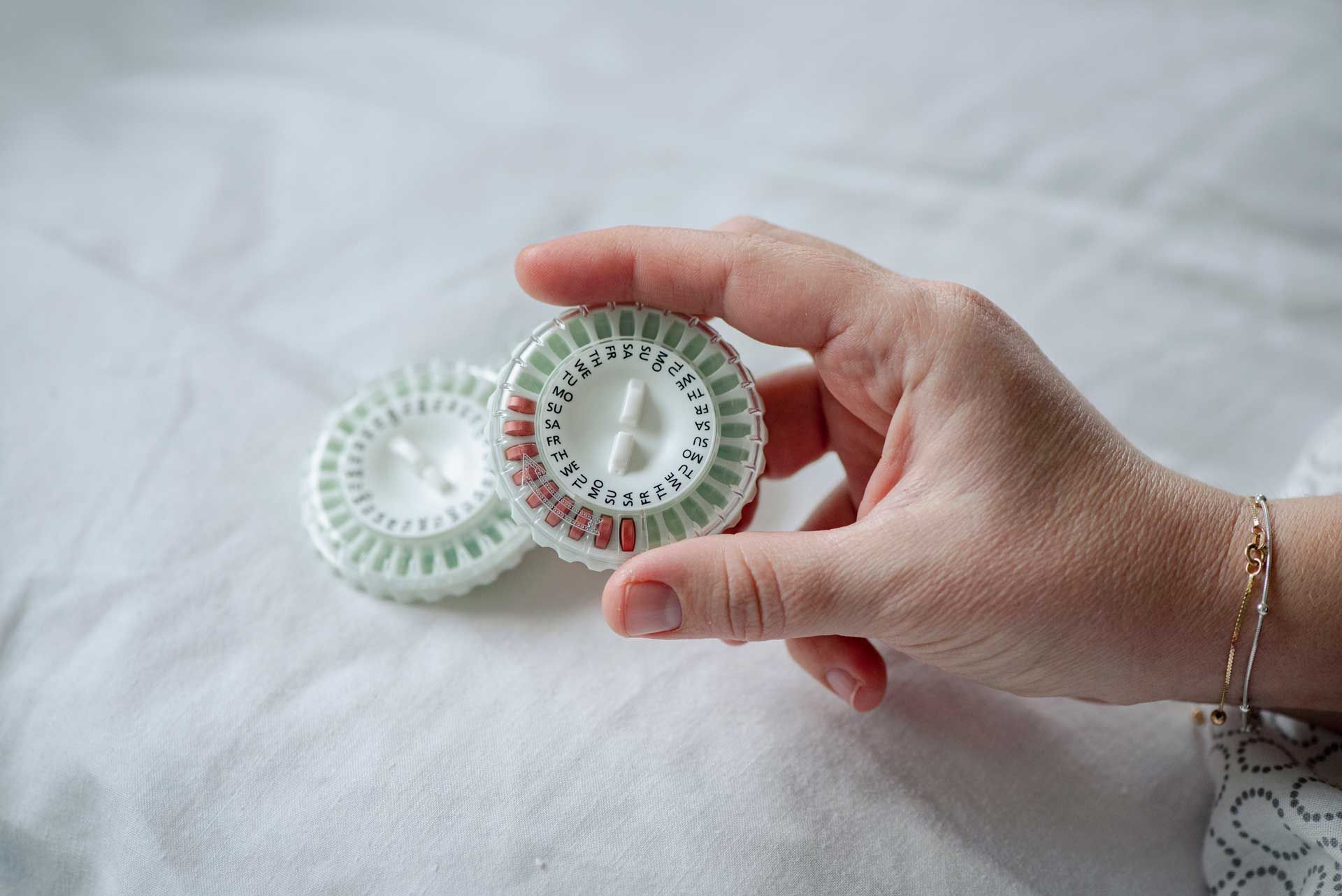 A hand holds a circular pill dispenser labeled with days, used for hormone therapy.