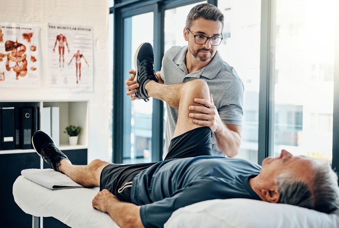 A physical therapist helping an elderly man with leg exercises on a treatment table in a clinic