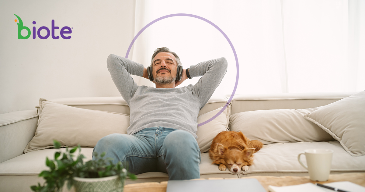 A man is sitting on a couch with a dog and listening to music.