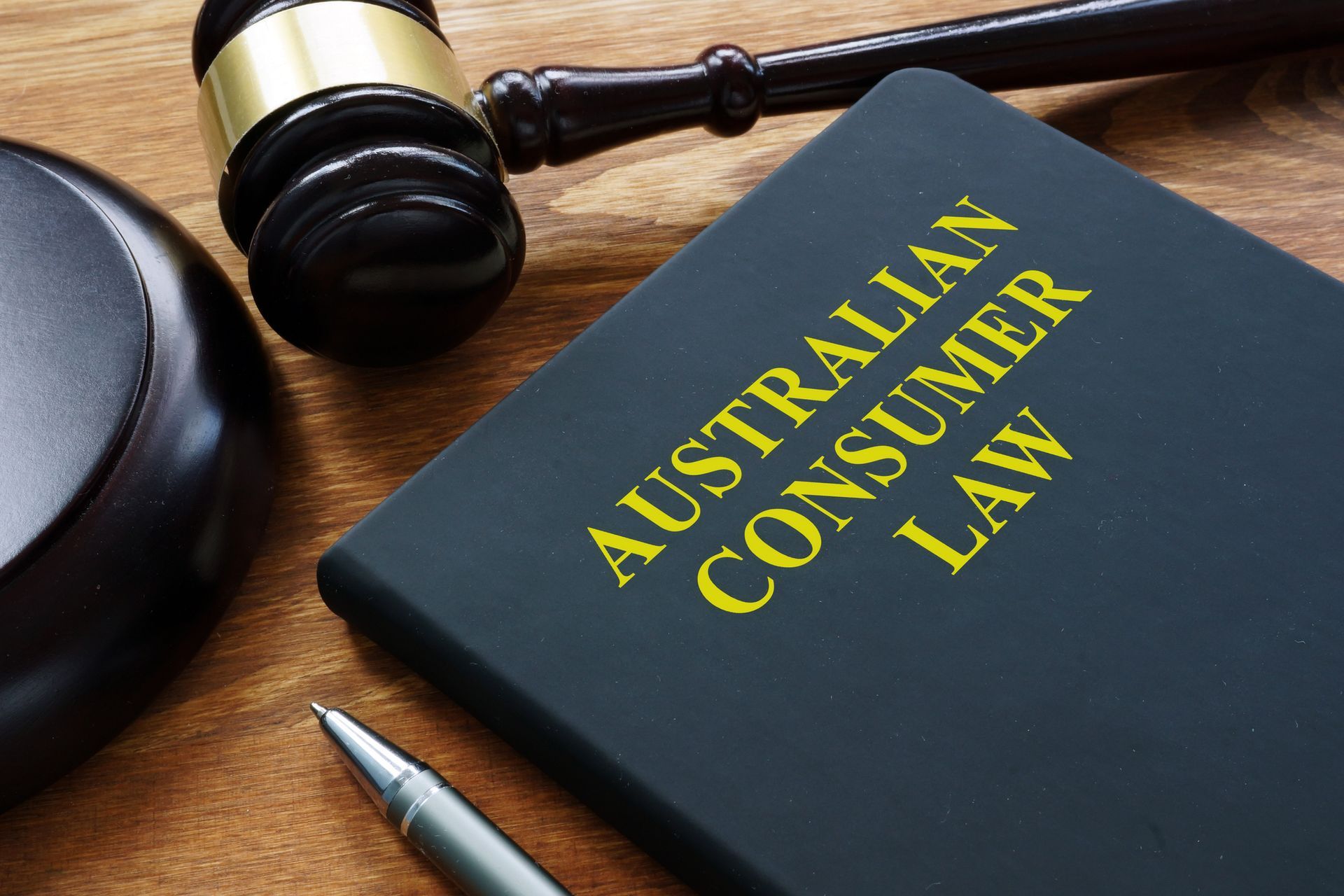A book titled australian consumer law sits on a wooden table next to a judge 's gavel and a pen.