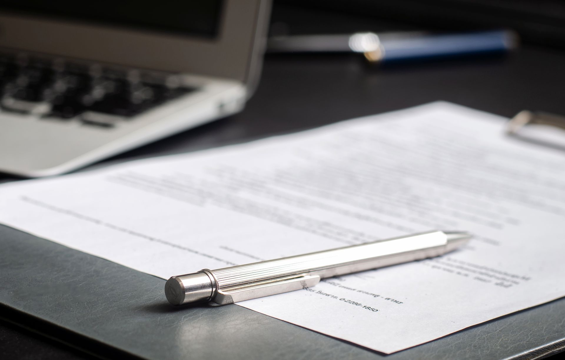 A pen is sitting on top of a clipboard next to a laptop.