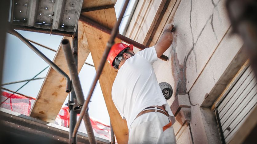 Operaio edile con casco, impegnato a riparare un muro esterno su un'impalcatura.