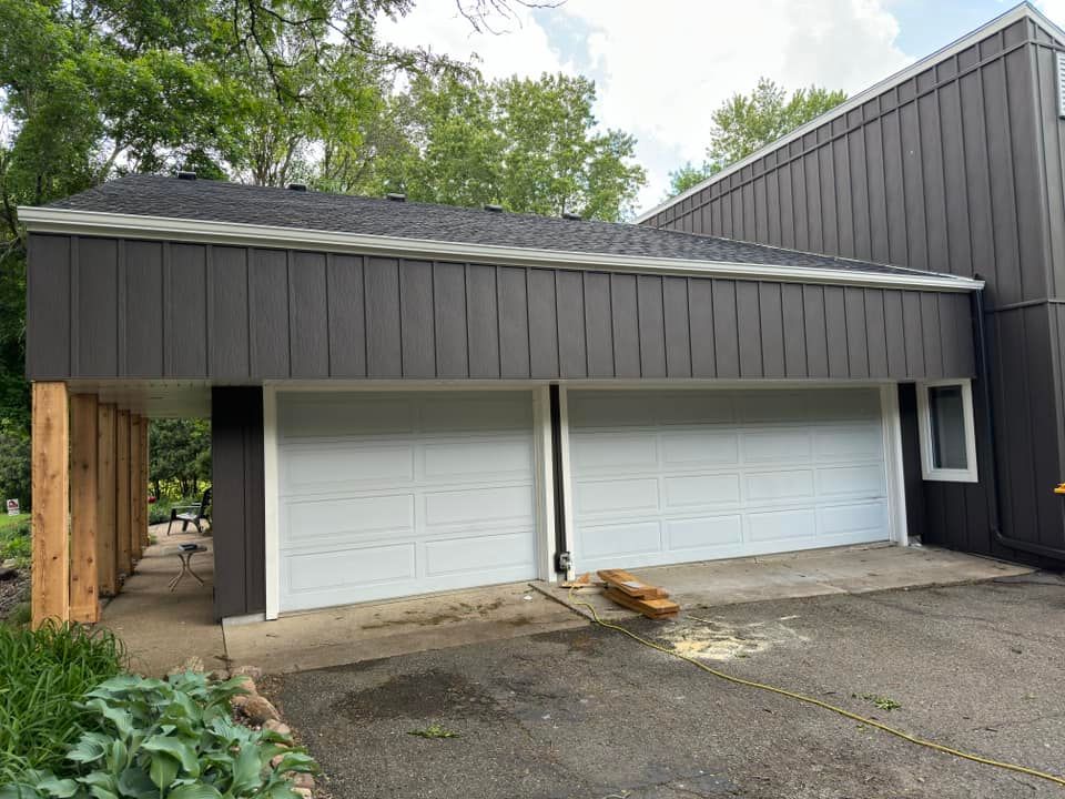 Two-car garage with white doors, gray siding, and a wooden fence.