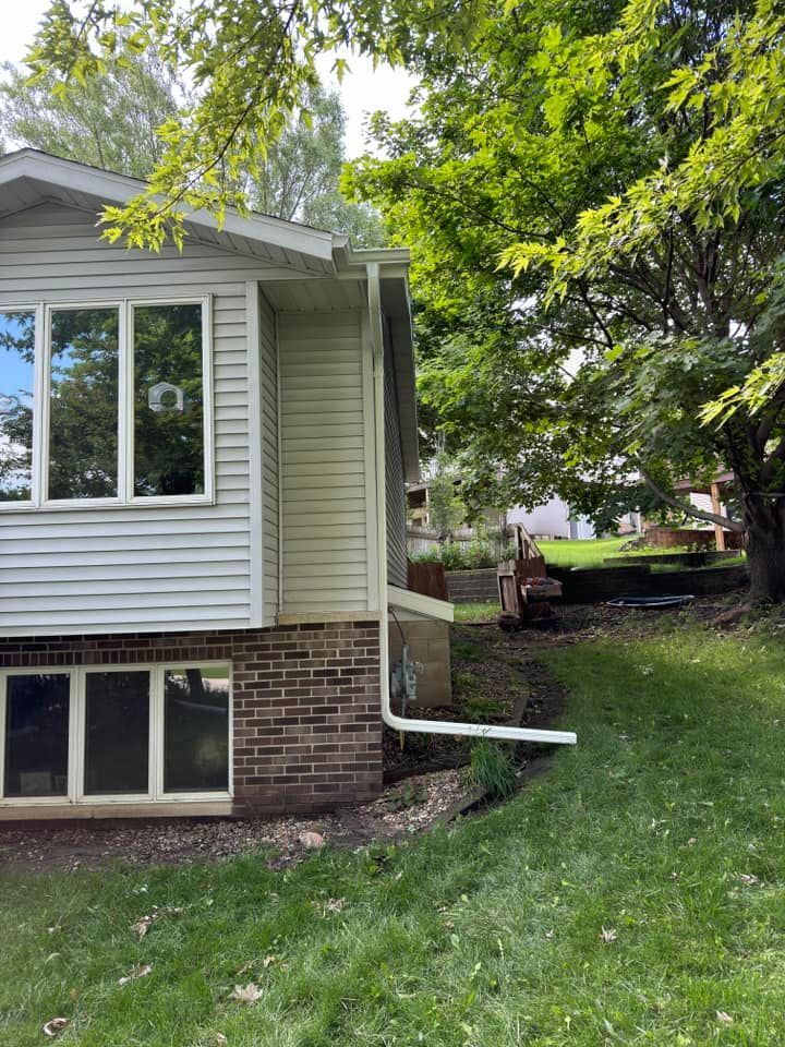 House exterior with white siding, brick foundation, gutters, and a tree on a sloped lawn.
