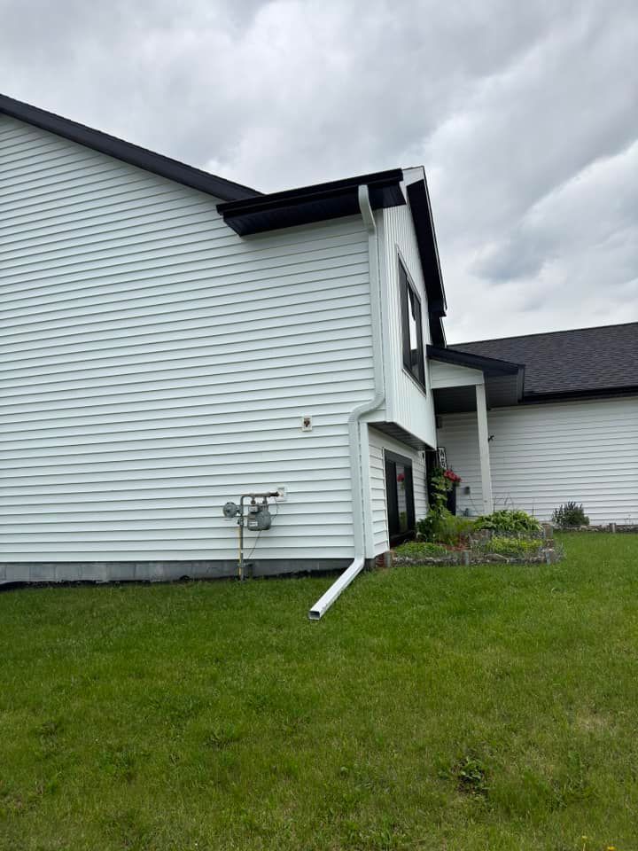 Side view of a white house with black trim, green lawn, and cloudy sky.