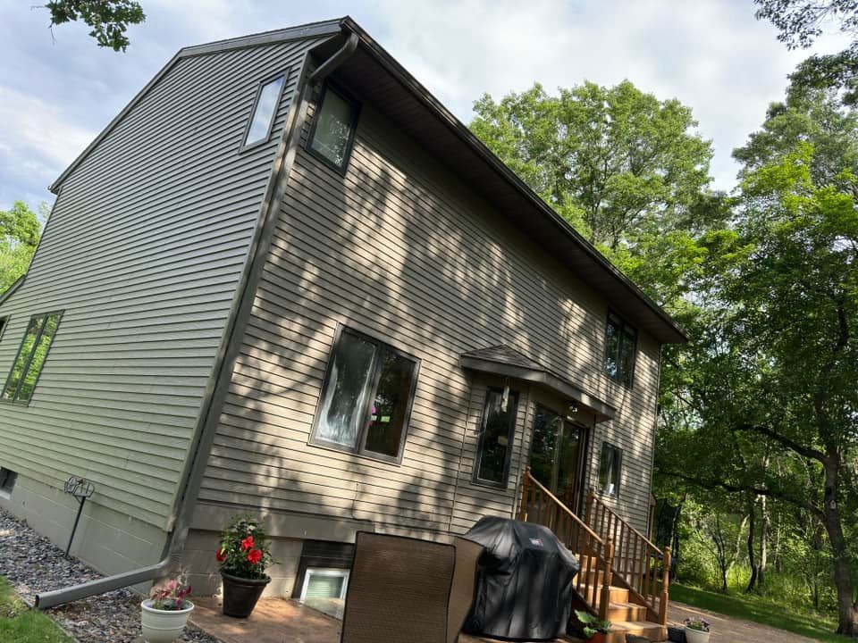 Two-story house with green siding, brown trim, and a small deck with a grill outdoors.
