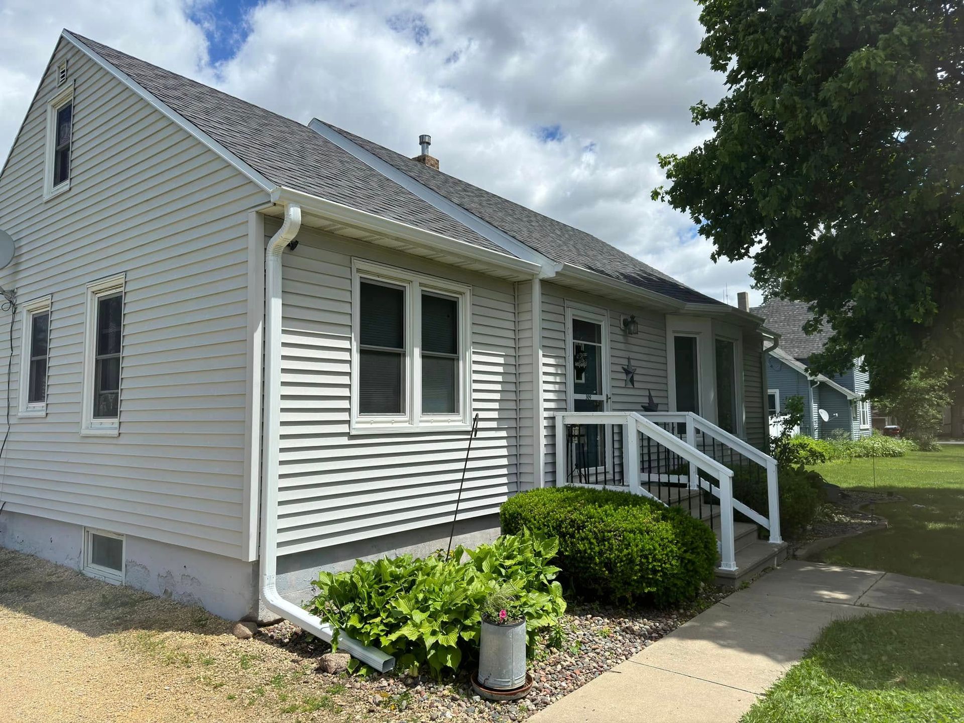 White house with gray roof, front porch, bushes, and a cloudy sky.