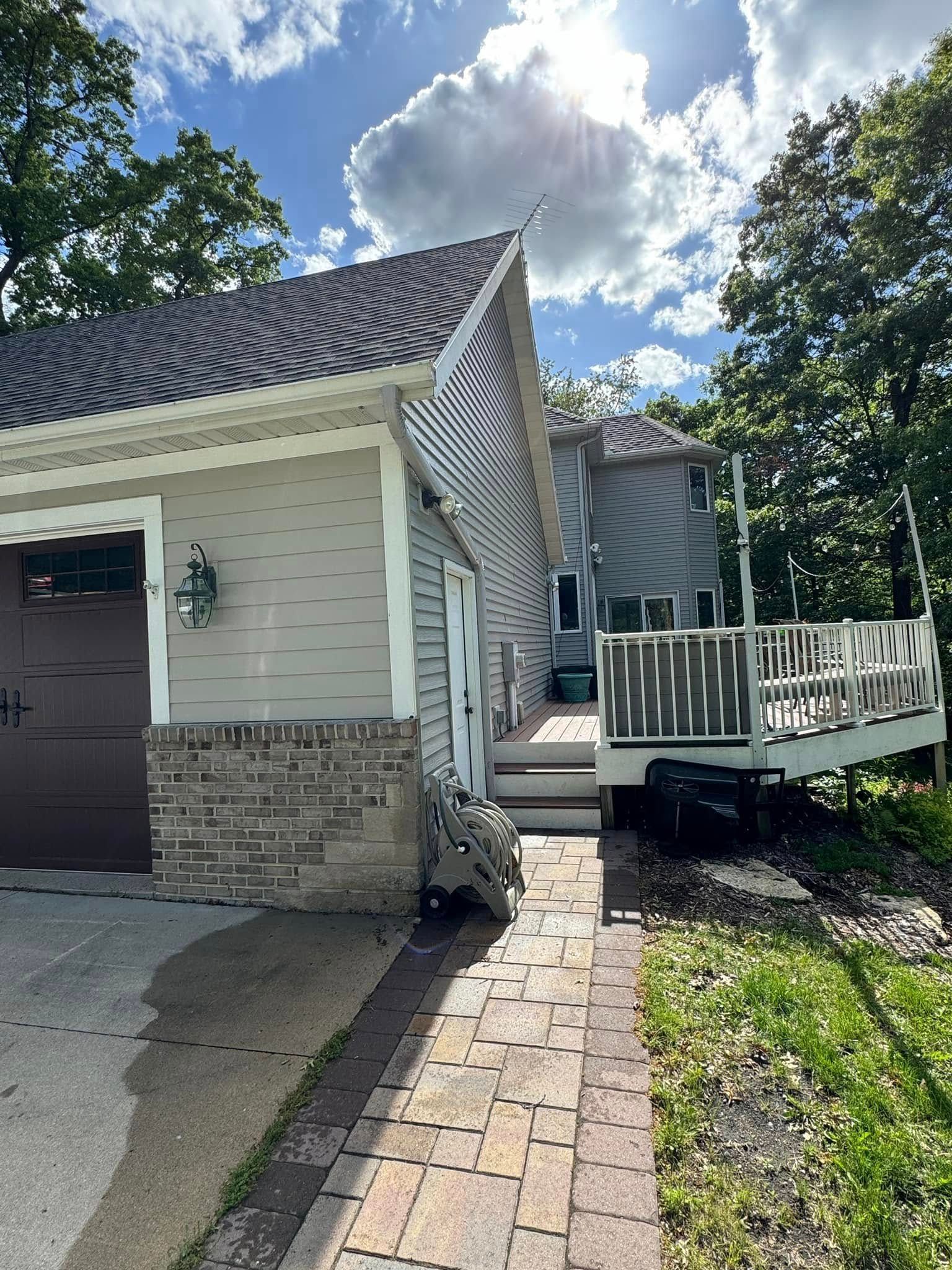 House exterior with garage, deck, and brick walkway under a sunny sky.