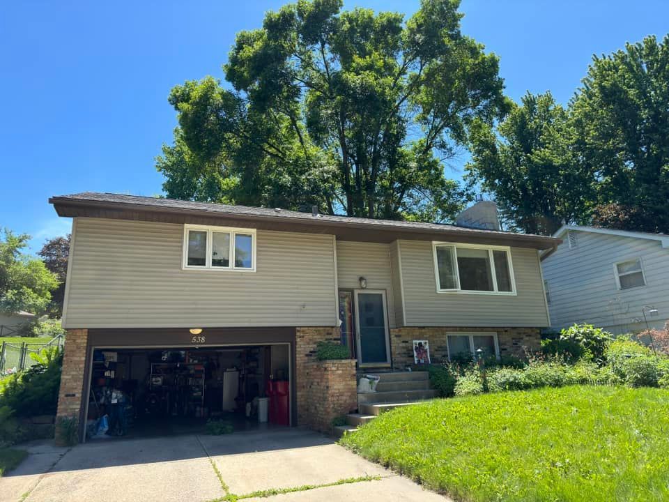 Tan two-story house with open garage, brick accents, and green lawn under a sunny sky.