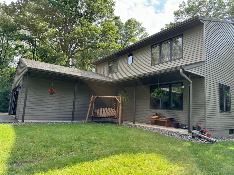 Green house with porch swing and lush lawn, surrounded by trees.