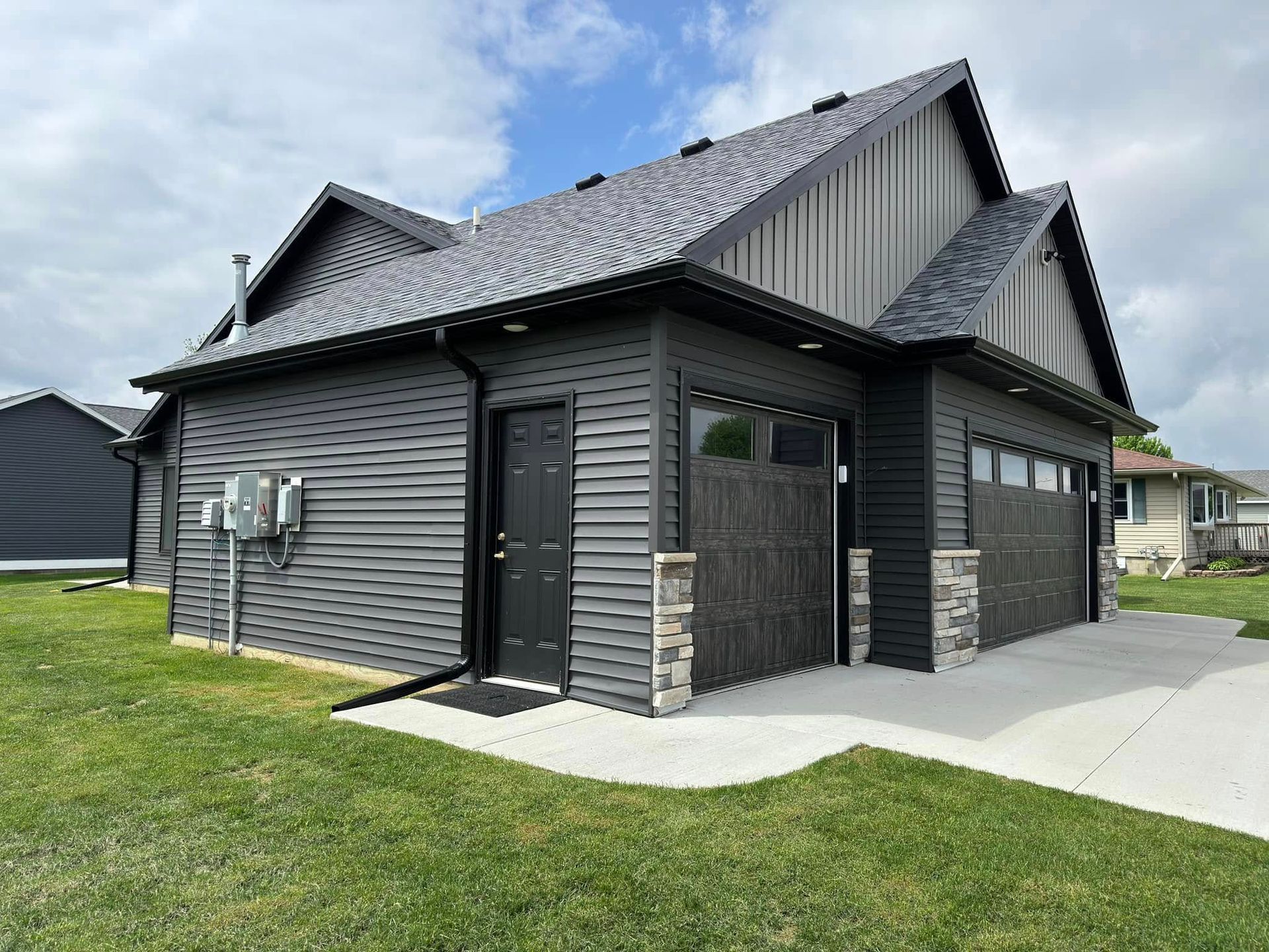 Black garage with gray stone accents and matching black door and garage doors, on a green lawn.