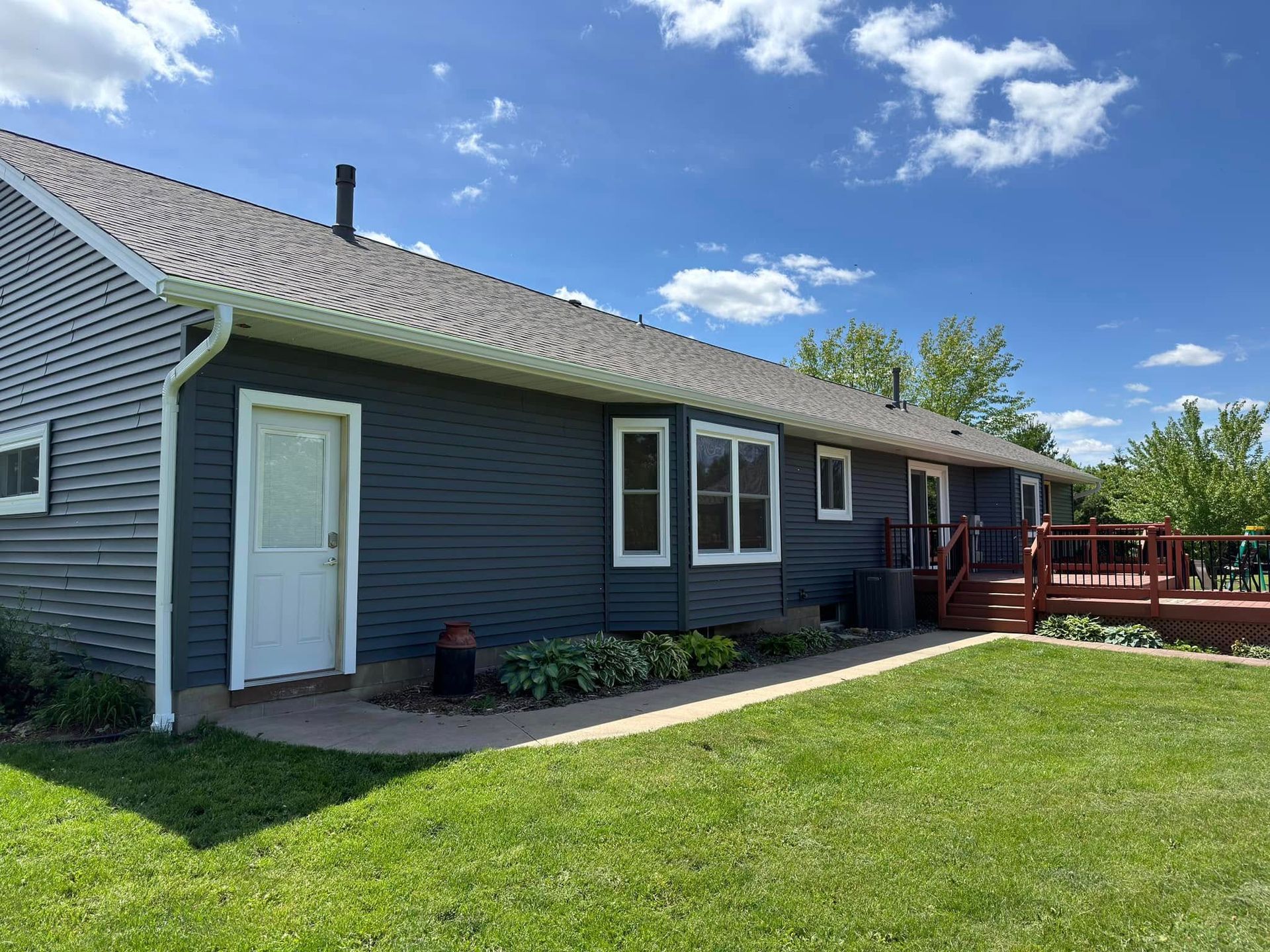 House with blue siding, white door and trim, red deck, green lawn, under a blue sky.