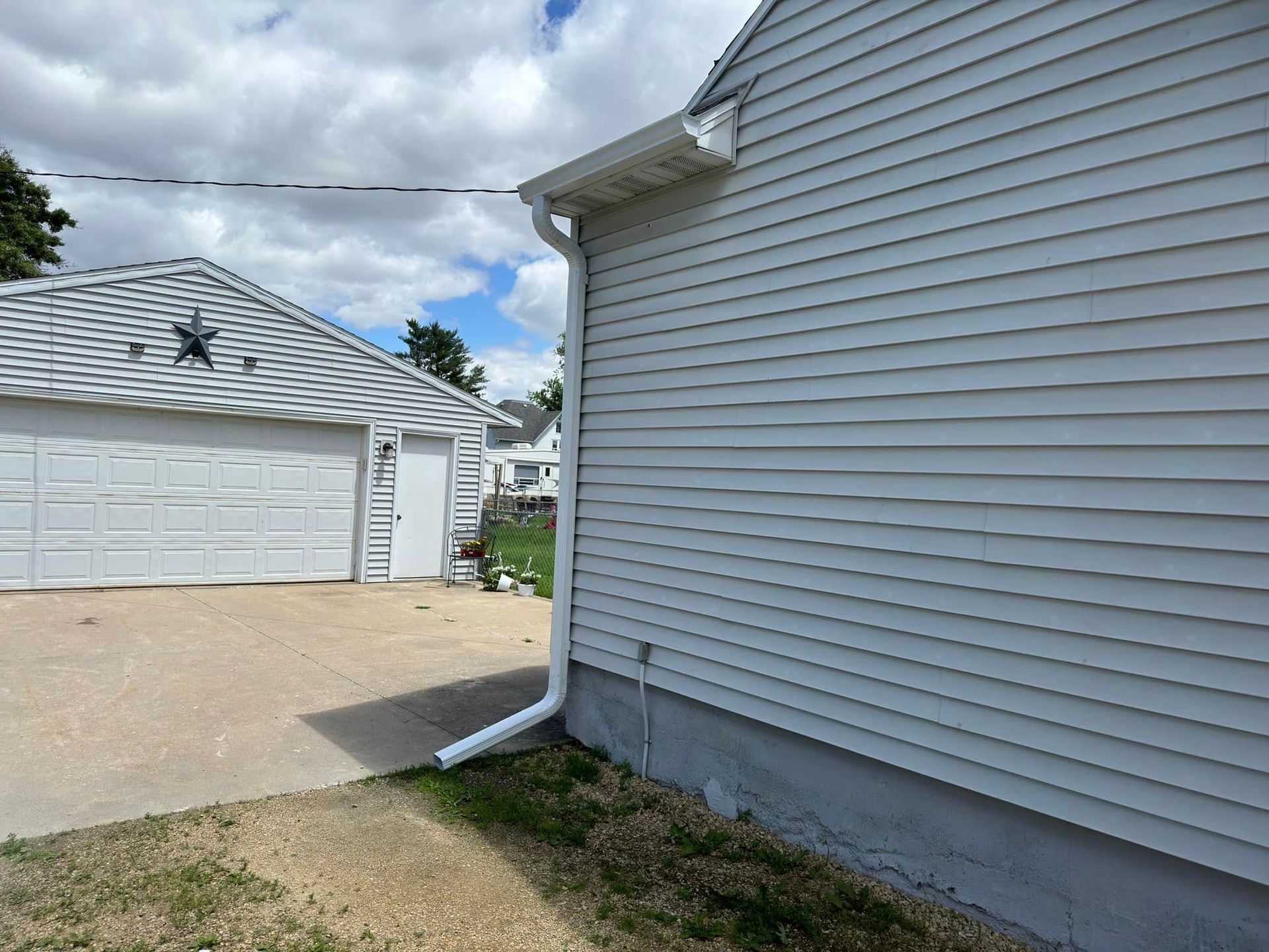 White house siding with gutter and downspout, driveway, and detached garage on a partly cloudy day.