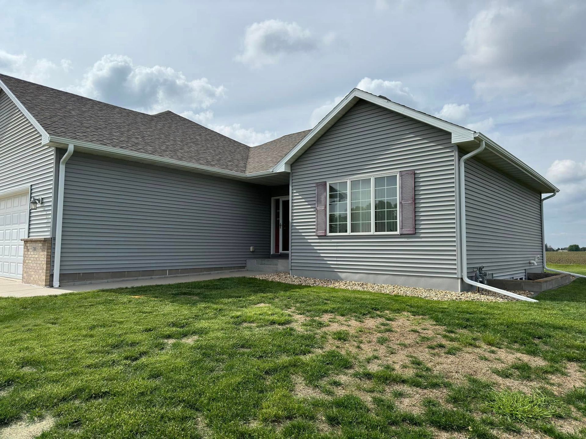 Gray house with matching siding, brown roof, and green lawn under a cloudy sky.