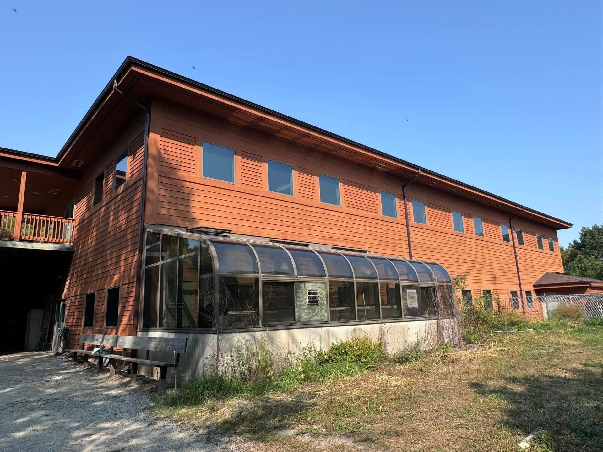 Two-story brick building with a greenhouse and wooden accents, under a clear blue sky.