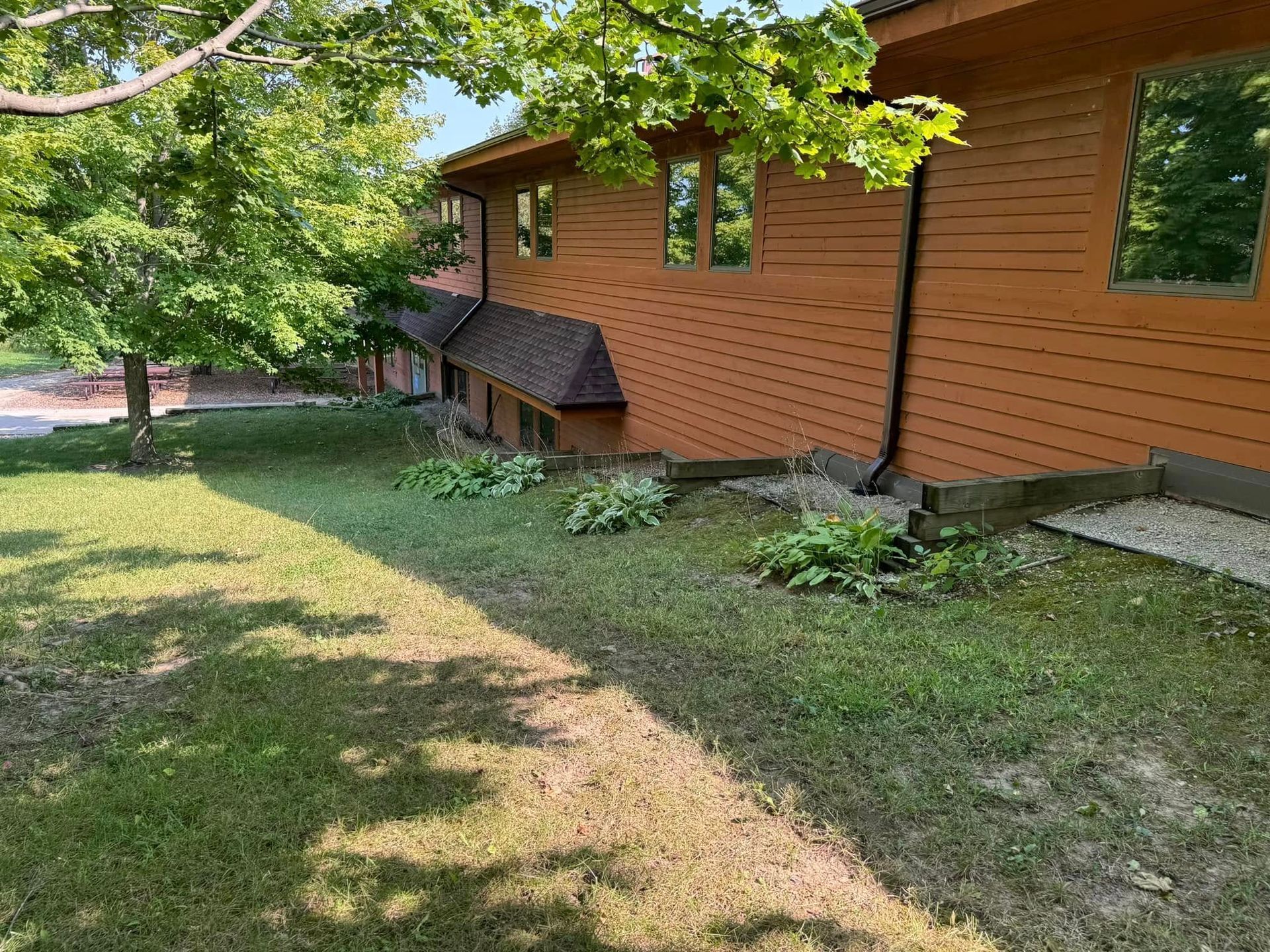 Brown house with windows and a dark roof, surrounded by green grass and a tree.